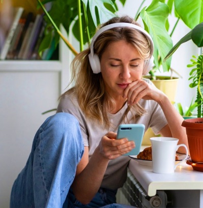Een Dame luistert naar de krant, met lichtblauwe smartphone en witte hoofdtelefoon.