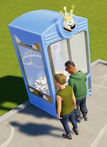 Twee mannen staan voor een blauwe Grijpmachine, gevuld met King Coaster-knuffels. Op de achterwand staat het witte Planet Coaster-logo. De 'Grijper' zakt naar beneden.