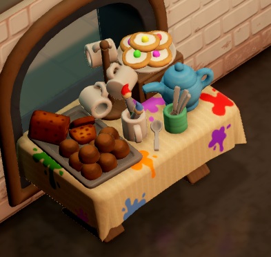 Tegen een venster in de Art Studio staat een tafel vol koekjes en cake, plus een tassenhouder met drie tassen eraan, en een theeketel. Het tafelkleed zit vol kleurige verfvlekken.