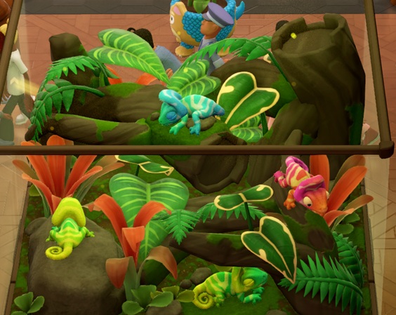 Vier Chamoodleons in hun Terrarium. Twee Chamoodleons zijn lichtgroen; ze liggen onderaan de foto. Bovenaan slaapt een lichtblauw exemplaar en rechts kruipt een roze Chamoodleon door de takken. Bovenaan wandelt een Bewaker voorbij.