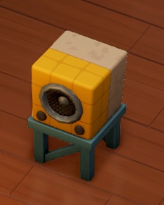 Op een blauw, houten verhoogje staat een kubusvormige luidspreker. De voorkant is geel en is opgebouwd uit negen kleine kubussen; de achterkant is grijswit en niet opgedeeld.